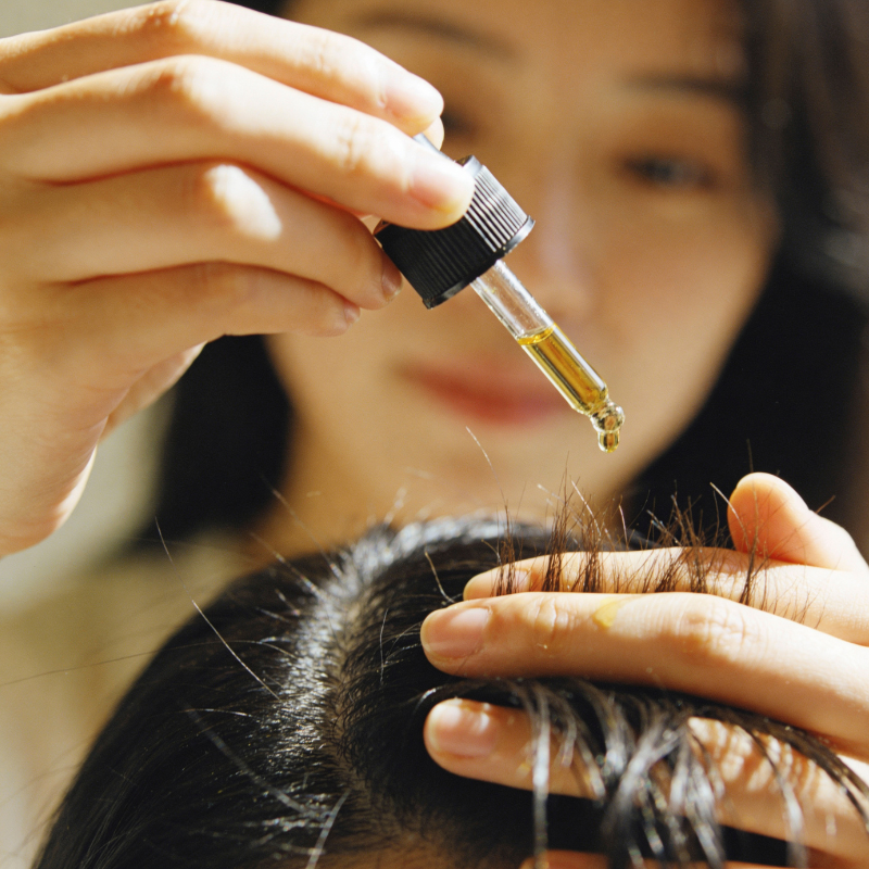 Woman applying herbal oil drops to scalp with a dropper